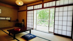 Una tipica stanza giapponese con pavimento in tatami, un tavolino basso, un cuscino e una porta scorrevole che dà su un patio esterno.