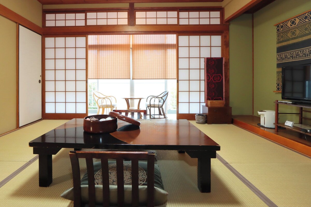 A traditional Japanese room with tatami flooring, a low table, and a TV on a stand.
