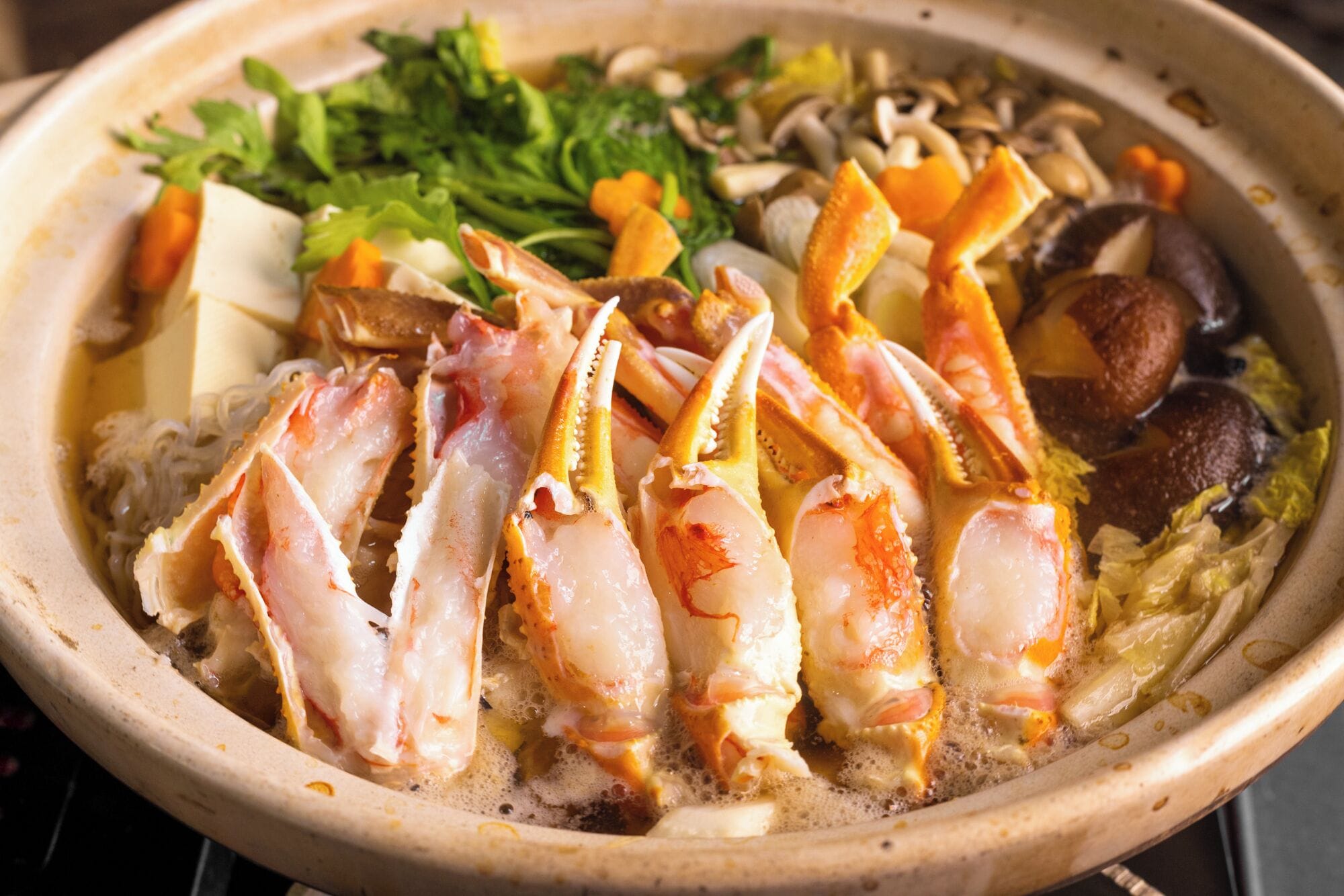 Un bol de soupe de fruits de mer contenant divers ingrédients, comme des morceaux de crabe, des champignons et des légumes verts à feuilles.