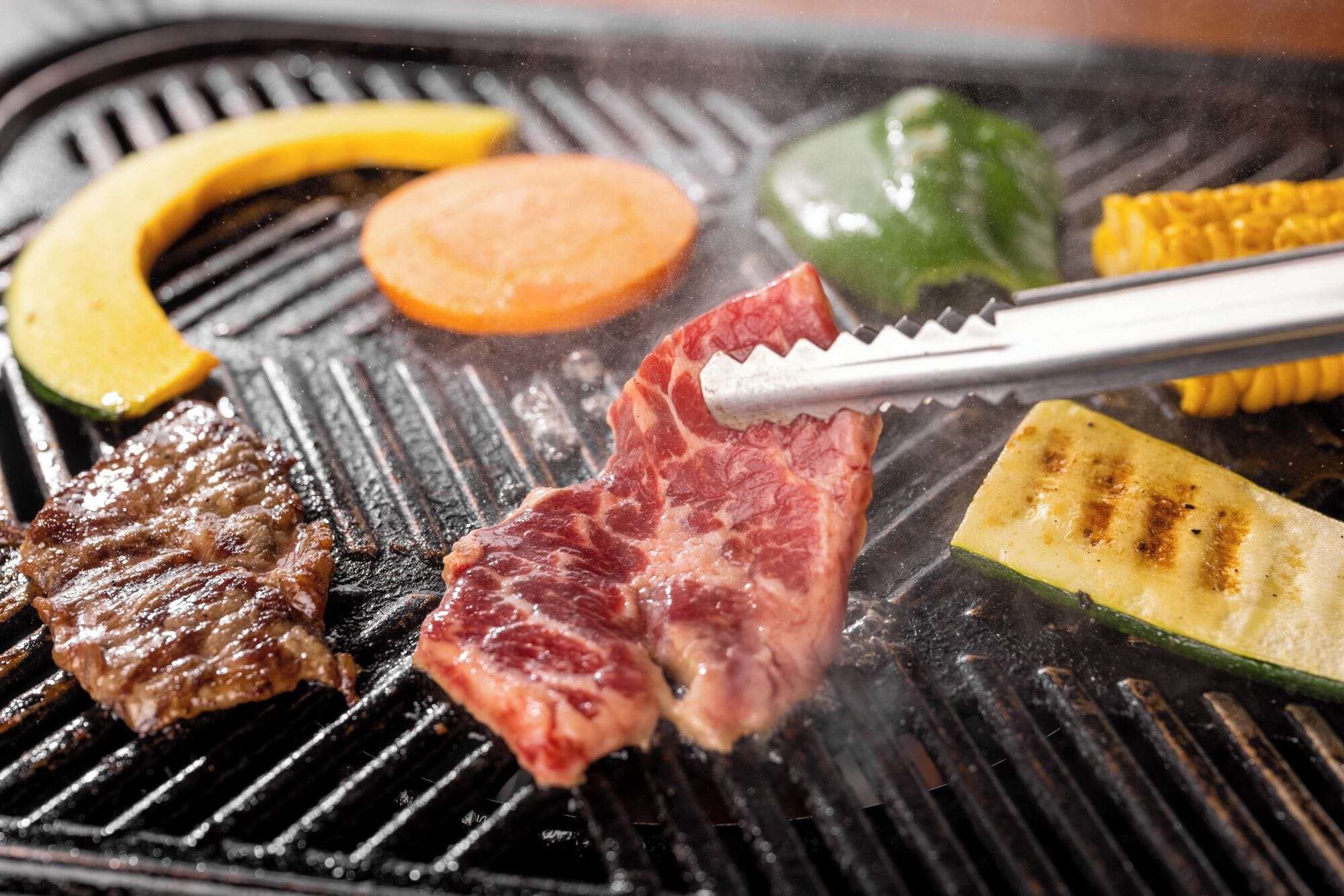 A grill with various meats and vegetables being cooked.