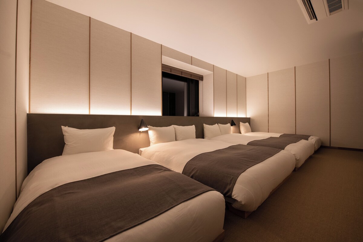 A hotel room with three beds, a large window, and a wall-mounted air conditioning unit.