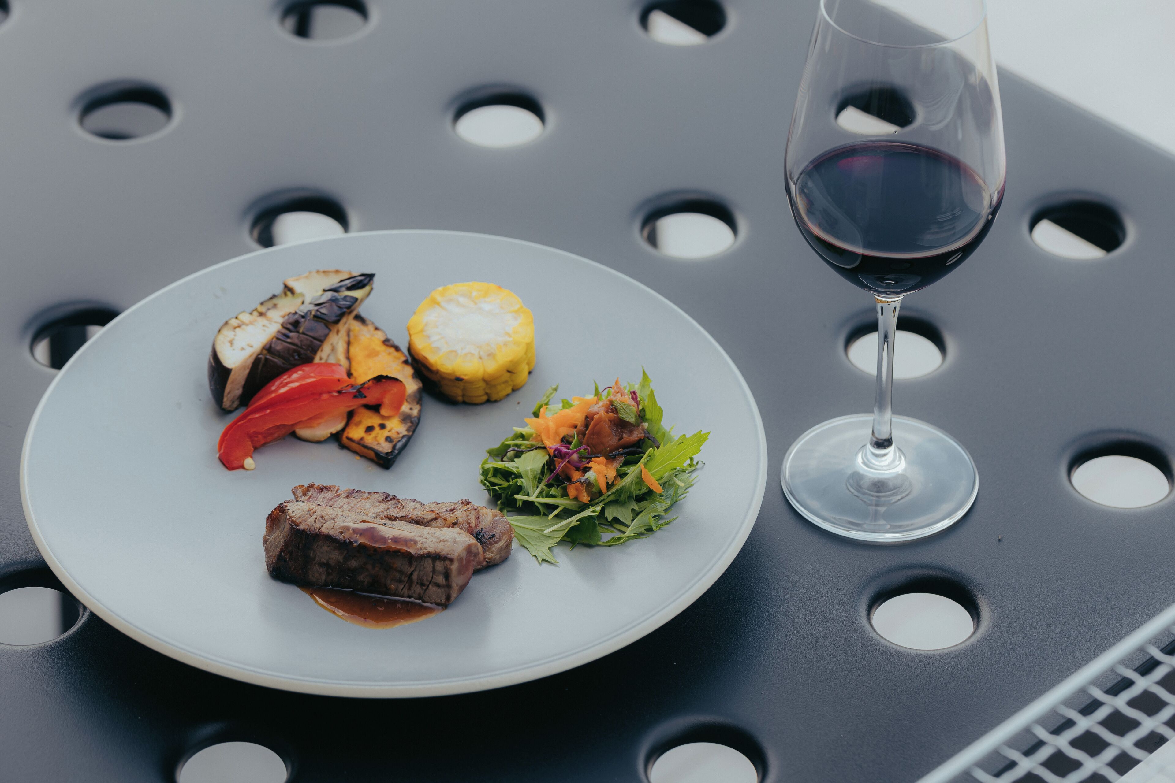 A plate of food with a glass of red wine on a table with circular cutouts.