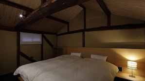 A bedroom with a wooden headboard, a single bed, a nightstand with a lamp, and a sloped ceiling with exposed beams. - Toutou Onzaki Machiya no Yado (Kurashiki)