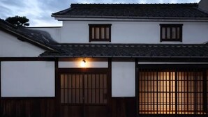 A traditional Japanese building with a tiled roof, wooden doors, and a lit lantern. - Toutou Onzaki Machiya no Yado (Kurashiki)