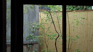 A room with a sliding glass door leading to a garden with a wooden fence, a table, and a chair. - Toutou Onzaki Machiya no Yado (Kurashiki)