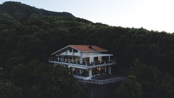 Una casa de dos pisos con techo de tejas rojas, rodeada por un bosque denso.