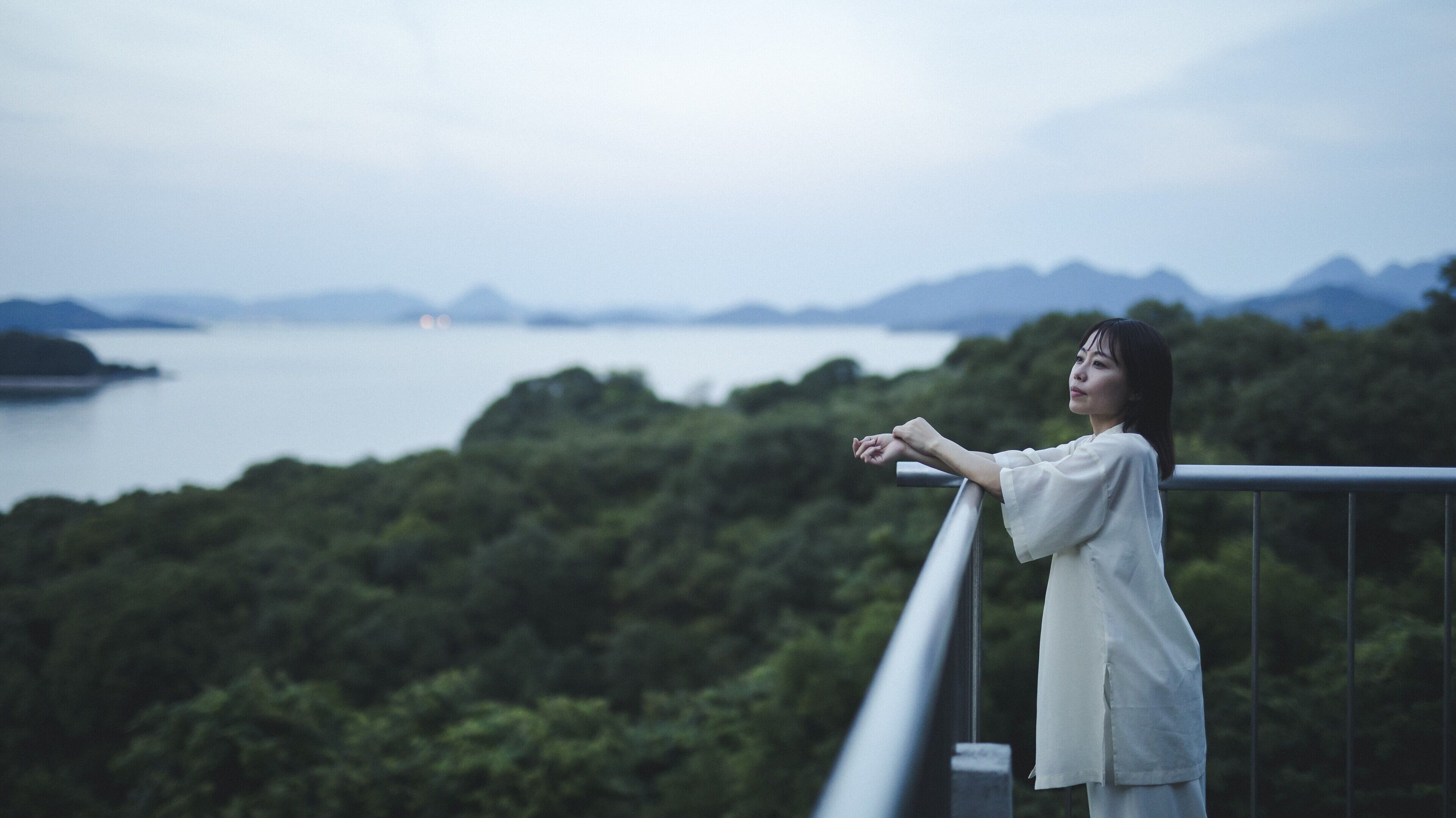 A person standing on a balcony overlooking a body of water and greenery.