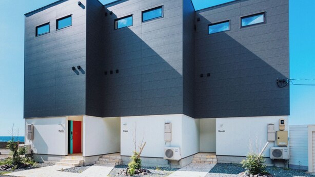 Un edificio moderno con techo plano, dos ventanas visibles y una puerta roja.