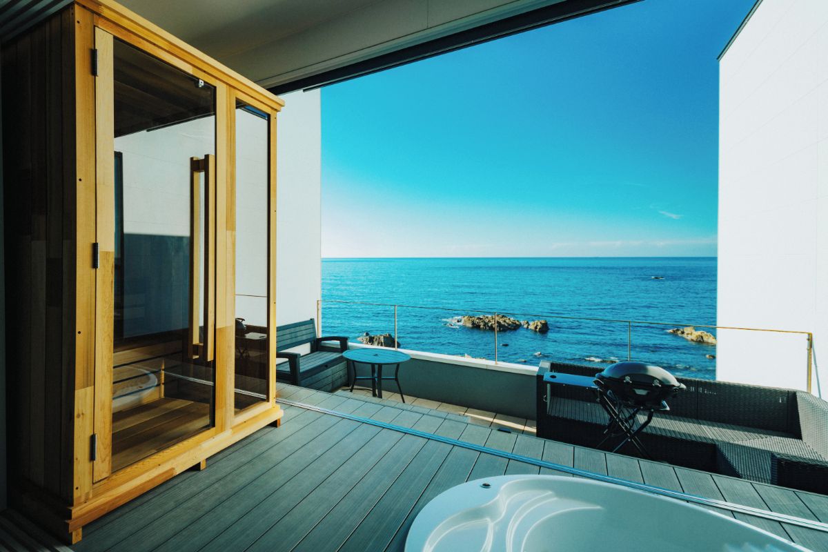 Un balcon avec vue sur la mer, un meuble en bois et des sièges d’extérieur.