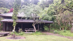 A traditional Japanese-style building with a tiled roof and a covered porch, surrounded by lush greenery and a well-maintained garden. - Sato no Yado Rishi (Isumi)