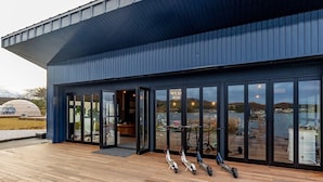 Een modern gebouw met grote glazen deuren, een houten terras en diverse elektrische scooters die er staan.