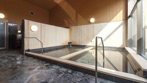 Un bain à remous doté d’un sol en pierre, de murs en bois et de rampes en métal.