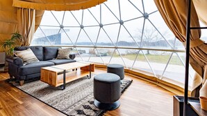 Een moderne woonkamer met een groot glazen dakraam, een zwarte leren bank, een houten salontafel en twee poufs.