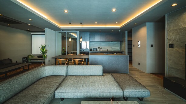 Una sala de estar moderna con un amplio sofá en forma de L, una zona de comedor con mesa de madera y una cocina con armarios grises y una isla central.