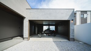 Un garaje moderno con un diseño elegante, una motocicleta en su interior y un camino de entrada de grava.