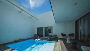 Un área de piscina interior moderna con techo de vidrio, sillas de descanso y una bañera de hidromasaje.