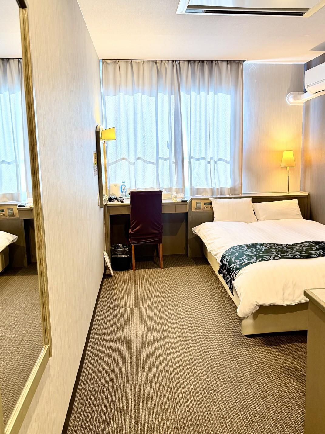 A hotel room with a bed, desk, chair, and a window with curtains.