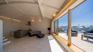 Una habitación de hotel moderna con cocina, zona de estar con sofá y mesa de centro, y un ventanal con vistas a la ciudad.
