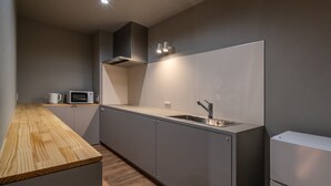 Cocina compacta con encimera de madera, microondas integrado, pileta de acero inoxidable y refrigerador pequeño.