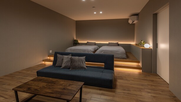 Un dormitorio moderno con un sofá, dos camas, una mesita de madera y una pequeña planta.