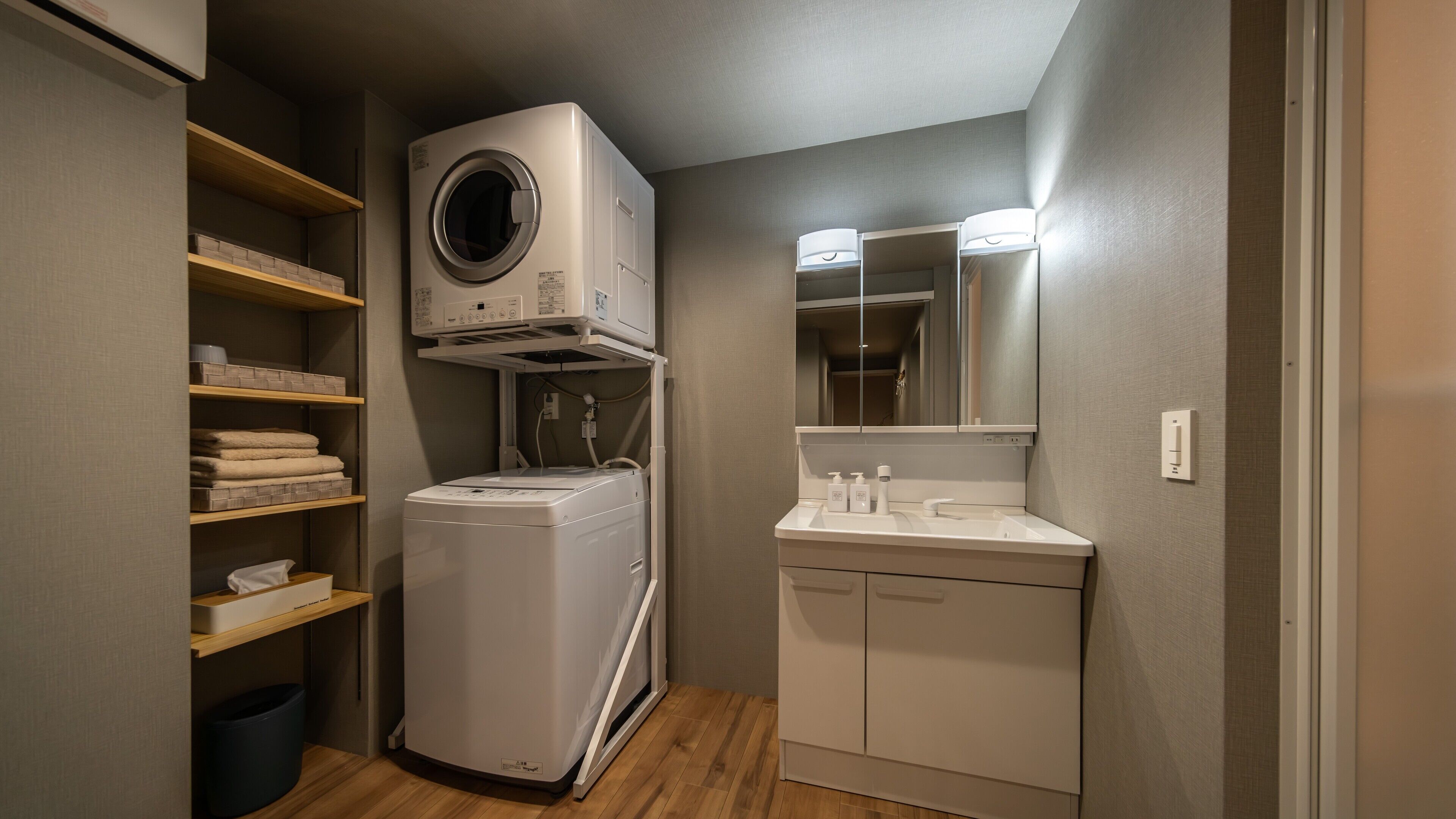 A compact laundry room with a front-loading washer and dryer, a small sink with a mirror, and shelves with folded towels.