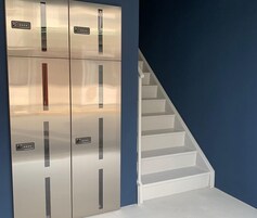Un conjunto de taquillas metálicas con un panel de control, junto a una escalera blanca frente a una pared azul.