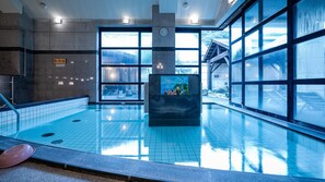 A swimming pool with clear glass walls, a clock, and a children's play area. - Kamegaike Onsen Kamenoyu Bettei (Ikata)