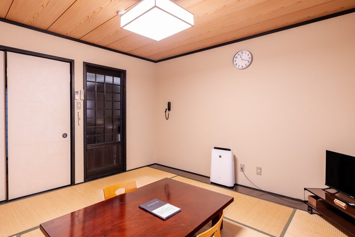 A conference room with a wooden table, chairs, a clock, and a television.