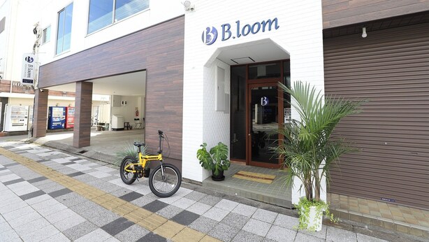 A B.loom hotel with a modern design, featuring a bicycle parked outside and potted plants near the entrance. - Business Hotel B.loom (Tanabe)