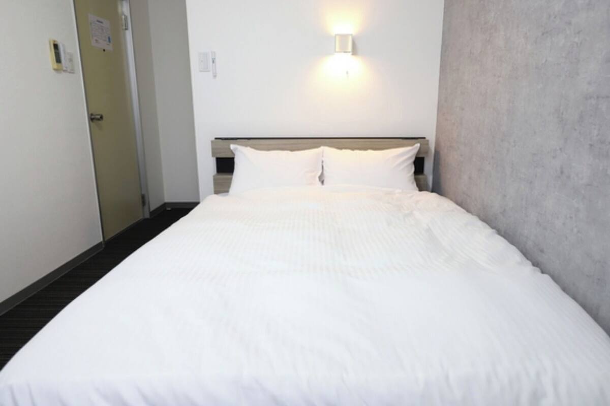 A hotel room with a bed, a wall-mounted light, and a door.
