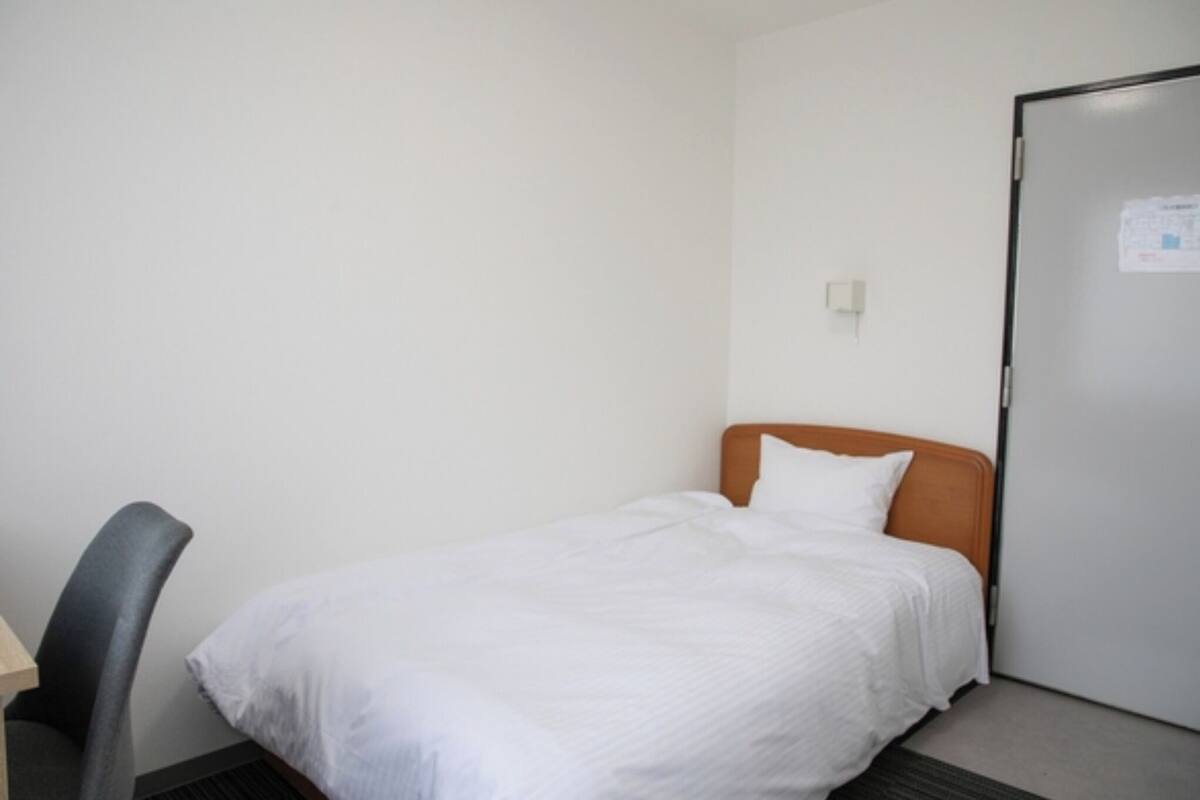 A small, single-bed room with a wooden headboard, a desk with a chair, and a white door with a notice on it.