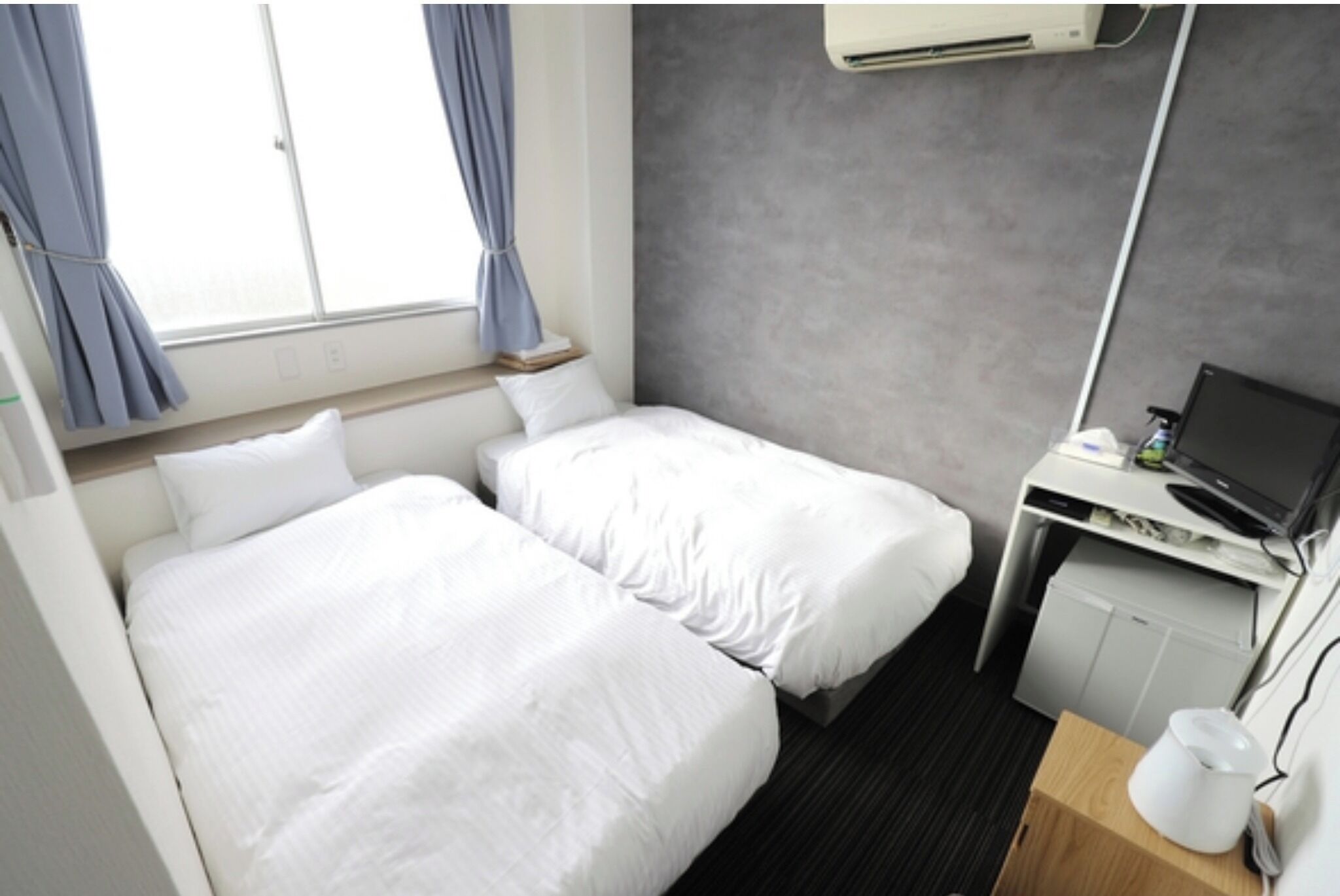 Habitación de hotel con dos camas, un escritorio con computadora y una kitchenette pequeña.