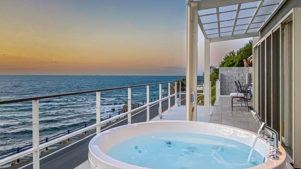 A balcony with a hot tub overlooking the sea, a glass railing, and outdoor seating. - Isola Terrace Awaji (Awaji)