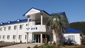 A hotel with a white facade, blue roof, and a sign in both English and Chinese. - Youhuuminnsyuku Beisaidoinn Kushimotokan (Kushimoto)