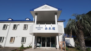 Uma Pousada Bayside com fachada branca, detalhes azuis e entrada central com portas de vidro.