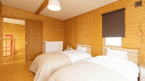 Ein Schlafzimmer mit Holzwänden, zwei Betten, einer weißen Kommode und einem Fenster mit Jalousie.