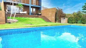 Ein modernes Haus mit Swimmingpool, einer Holzterrasse und einem Lounge-Bereich mit Gartenmöbeln.