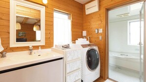 Ein modernes Badezimmer mit Holzwänden, einem großen Spiegel, einem Waschbecken, einer Waschmaschine und einer Duschkabine aus Glas.