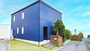 A blue building with a flat roof, a small entrance, and a wooden planter with a tree. - Awaji Beach House (Awaji)