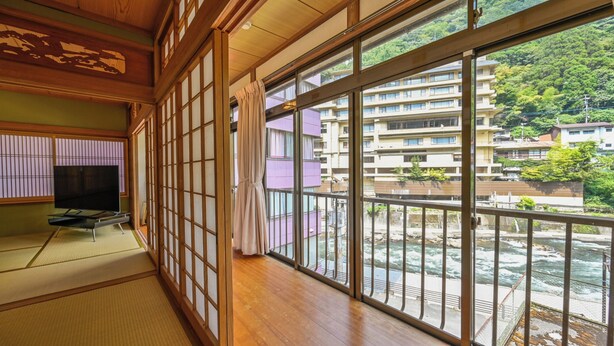 A traditional Japanese room with tatami flooring, a television, and a view of a river and buildings.