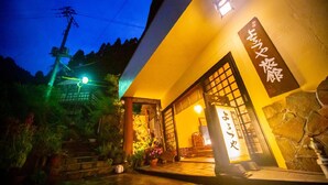 A traditional Japanese building with a stone entrance, a wooden gate, and a signboard with Japanese characters.