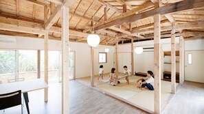 A spacious room with a high wooden ceiling, tatami mat flooring, and a sliding door leading to an outdoor area. - Denpaku Kakeroma Osai (Setouchi)
