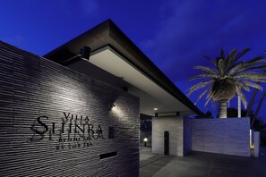Een modern gebouw met een bord waarop 'YILMA SHINTRA' staat en een palmboom.