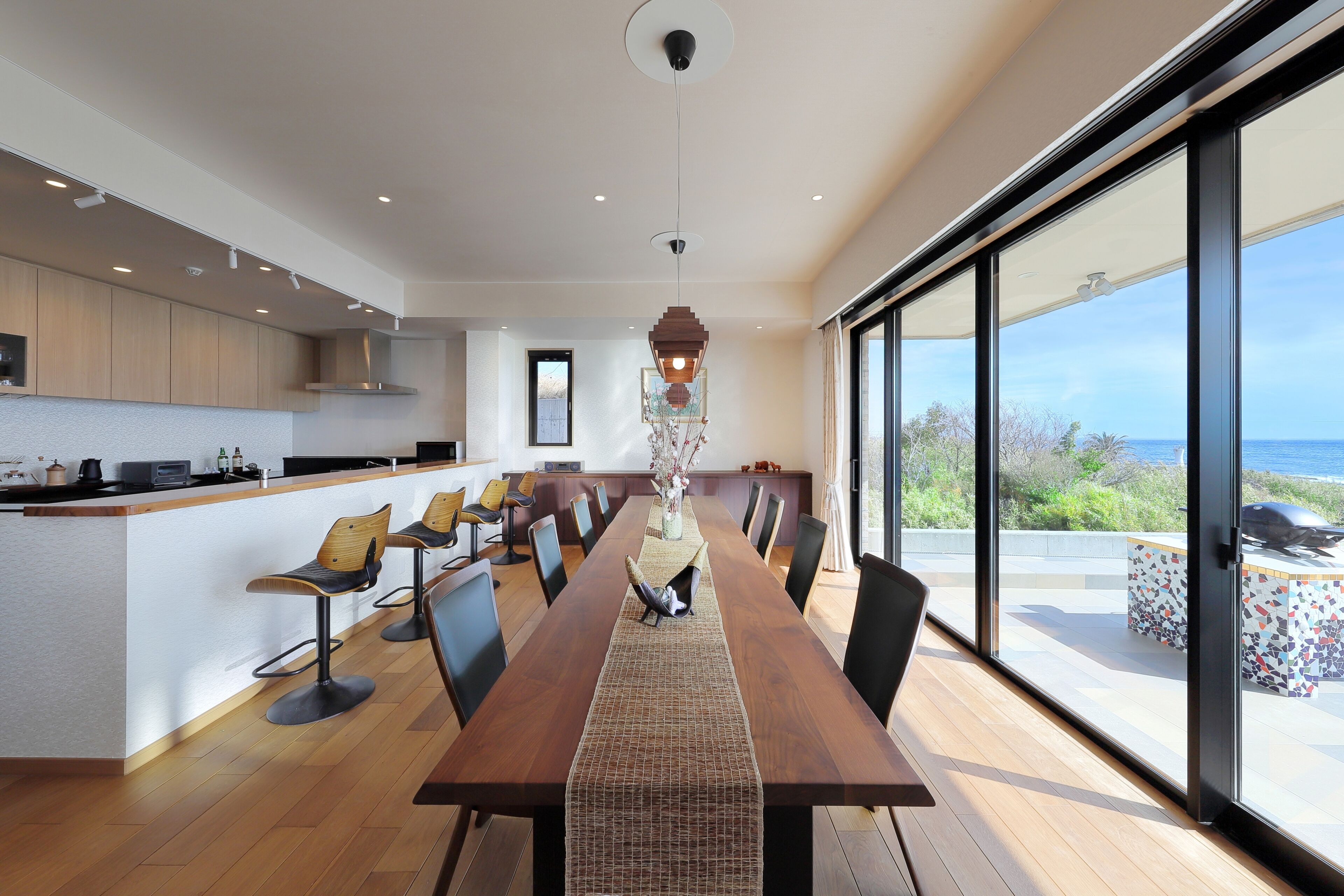 A modern kitchen with a long dining table, chairs, and a view of the outdoors.