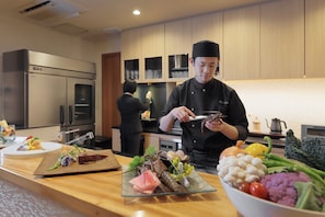 Een kok bereidt eten in een moderne keuken met roestvrijstalen apparatuur en houten kasten.