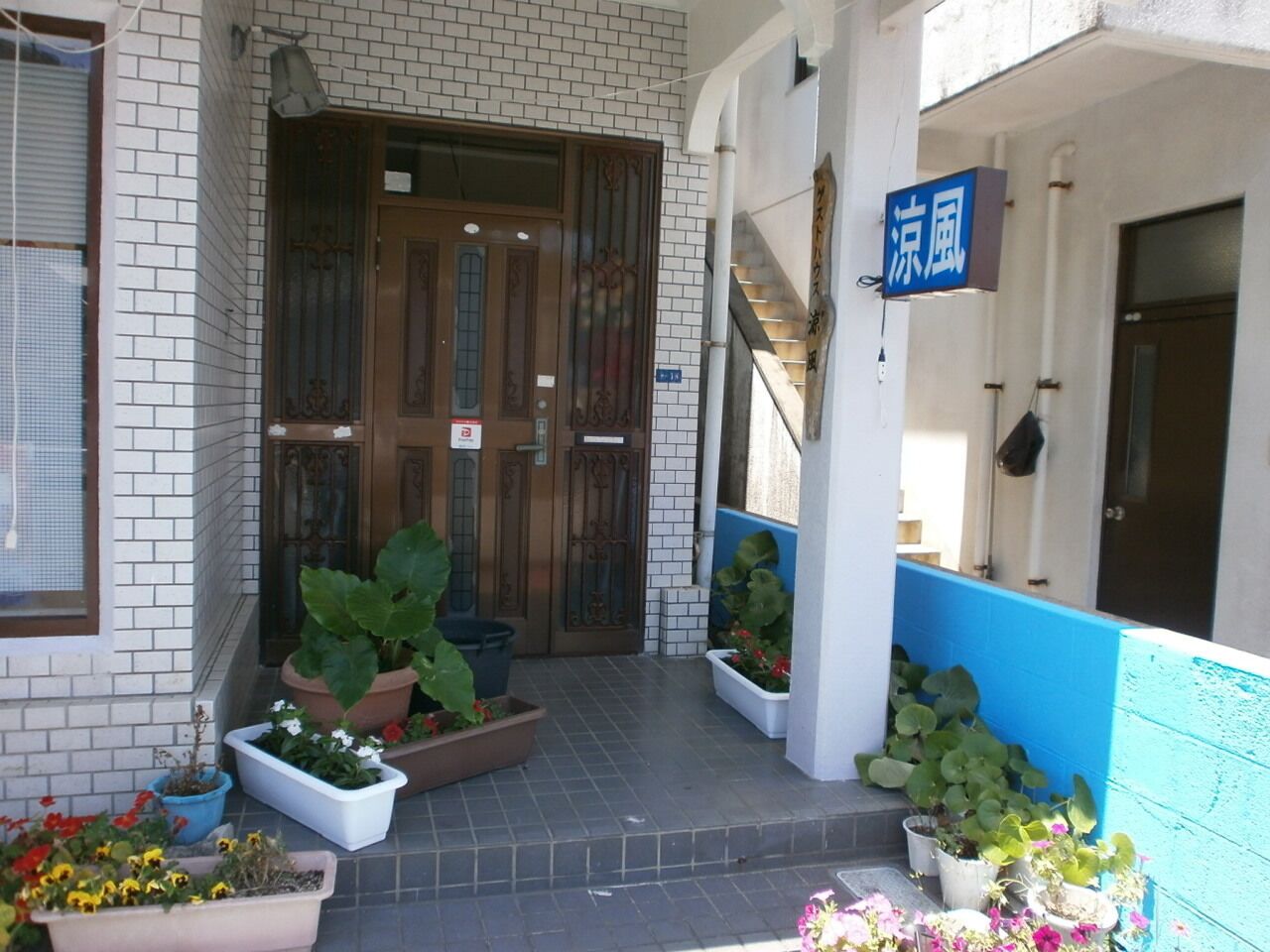 A building entrance with a tiled facade, a wooden door, and potted plants.