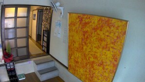 A hallway with a large abstract painting, a door with a calendar, and a fan mounted on the wall. - Guesthouse Ryofu (Amami)