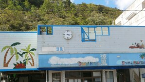 A building with a clock, a sign for 'GuestHouse', and a 'Shima Rentacar' sign. - Guesthouse Ryofu (Amami)