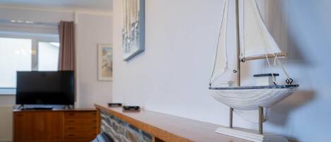 En modelsejlads på en træhylde, et fjernsyn og en stenvæg i et rum.
