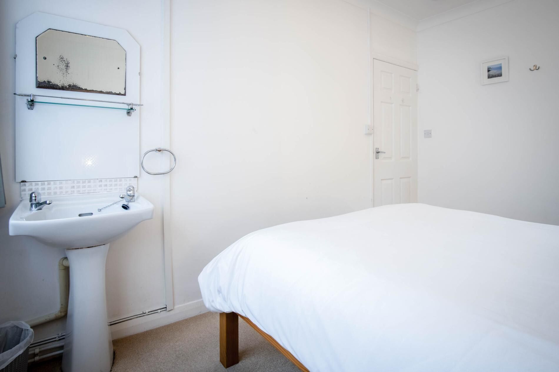 A bedroom with a single bed, a white sink, and a mirror above it.